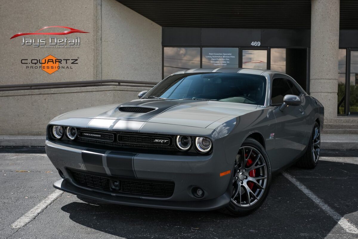 Gray Dodge Challenger with white racing stripe parked in front of a building.