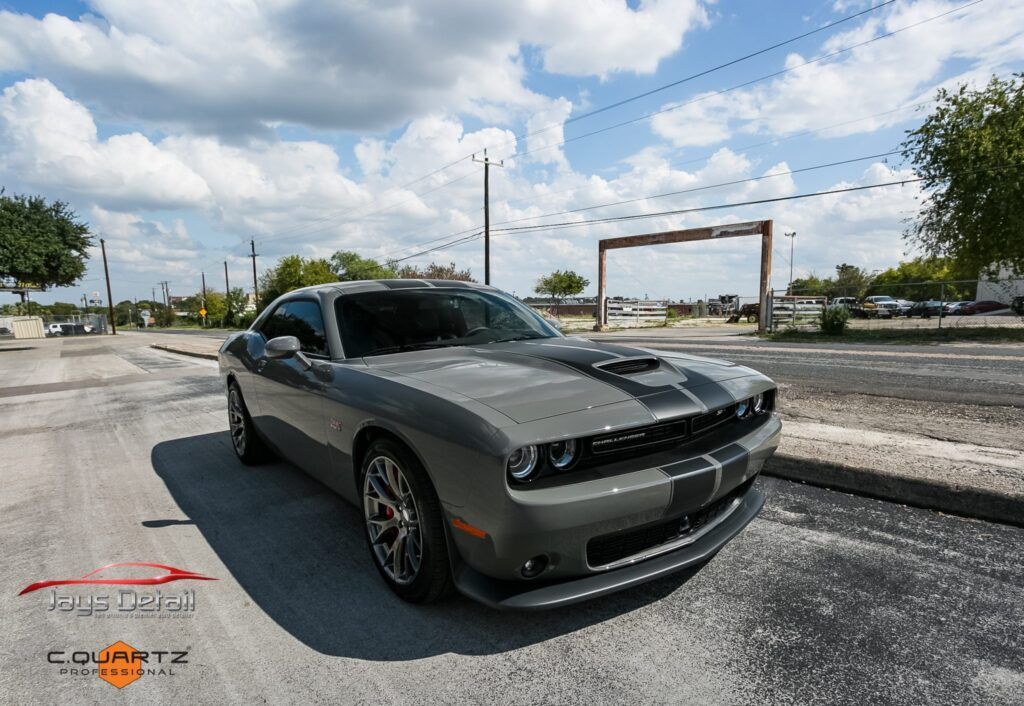 Gray Dodge Challenger with black stripes parked on a road, sunny day.