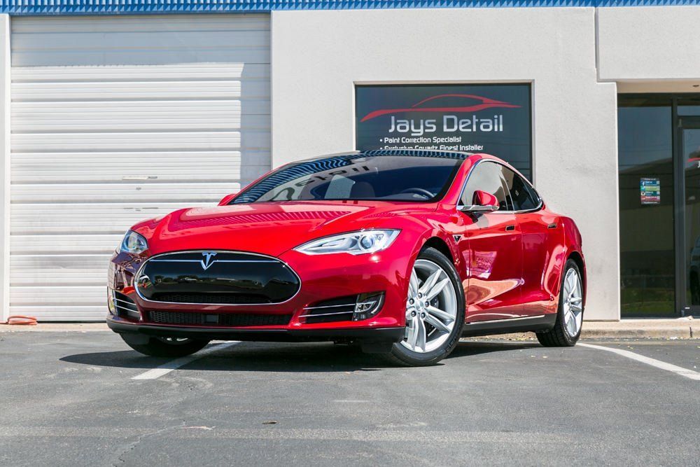 Red Tesla Model S parked outside a detail shop with the shop's logo visible.