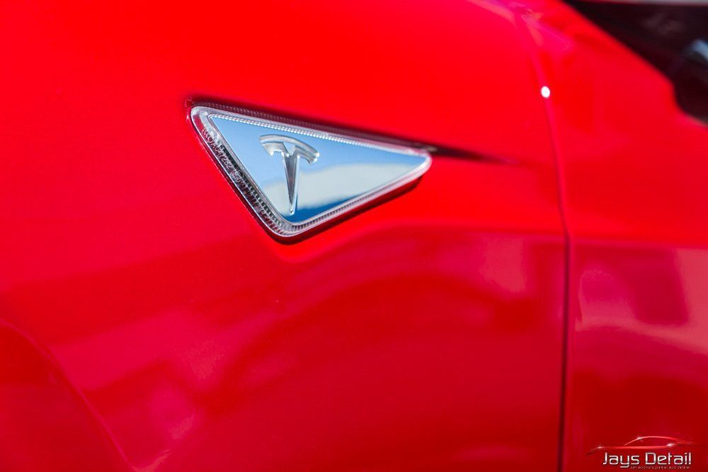Red Tesla car with silver emblem.
