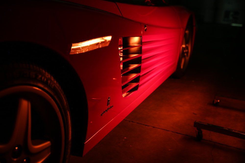 Red sports car side lit by red light, showing vents and wheel.
