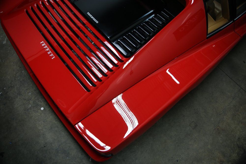 Red Ferrari sports car, close-up detail of the hood, side, and rear vents. Shiny, smooth finish.