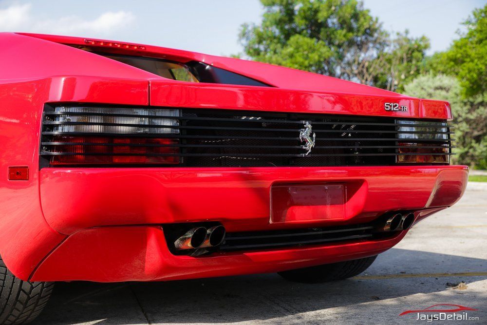 Red Ferrari Testarossa's rear view, showing black grill, dual exhaust, and Ferrari logo.