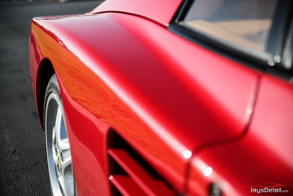Red Ferrari sports car, close-up of its side and rear, showing body curves and louvers.