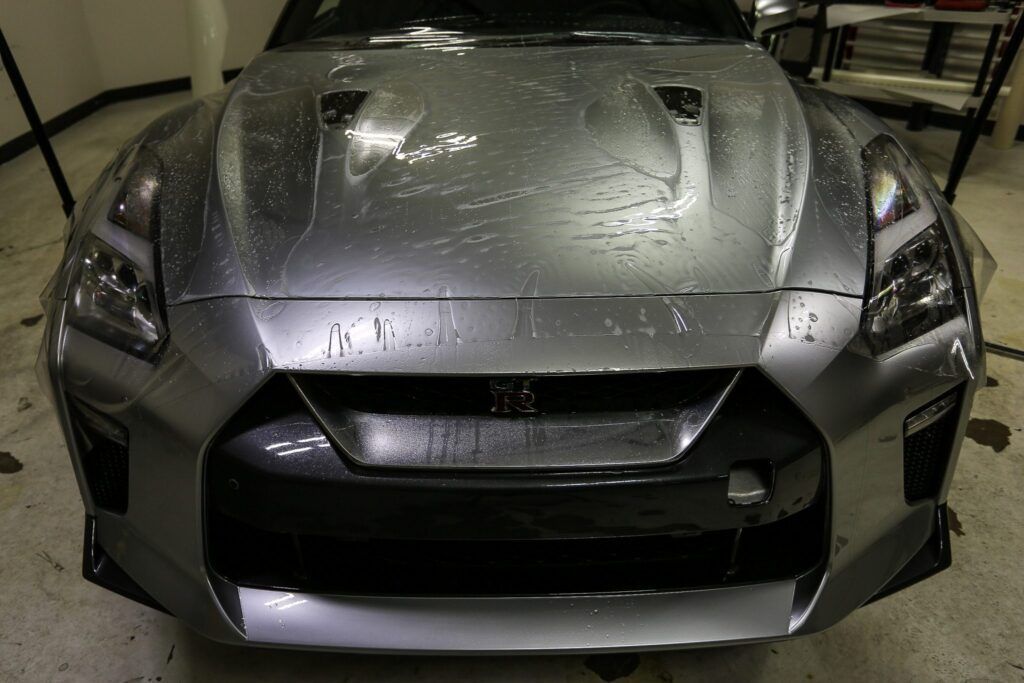 Silver Nissan GT-R sports car with water droplets on the hood, front view.