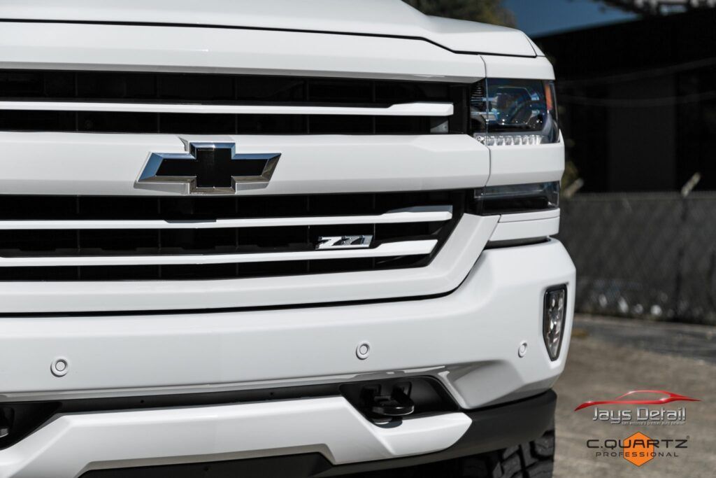 White Chevrolet Silverado truck, close-up of the front grille and bumper, with the Chevrolet logo in the center.