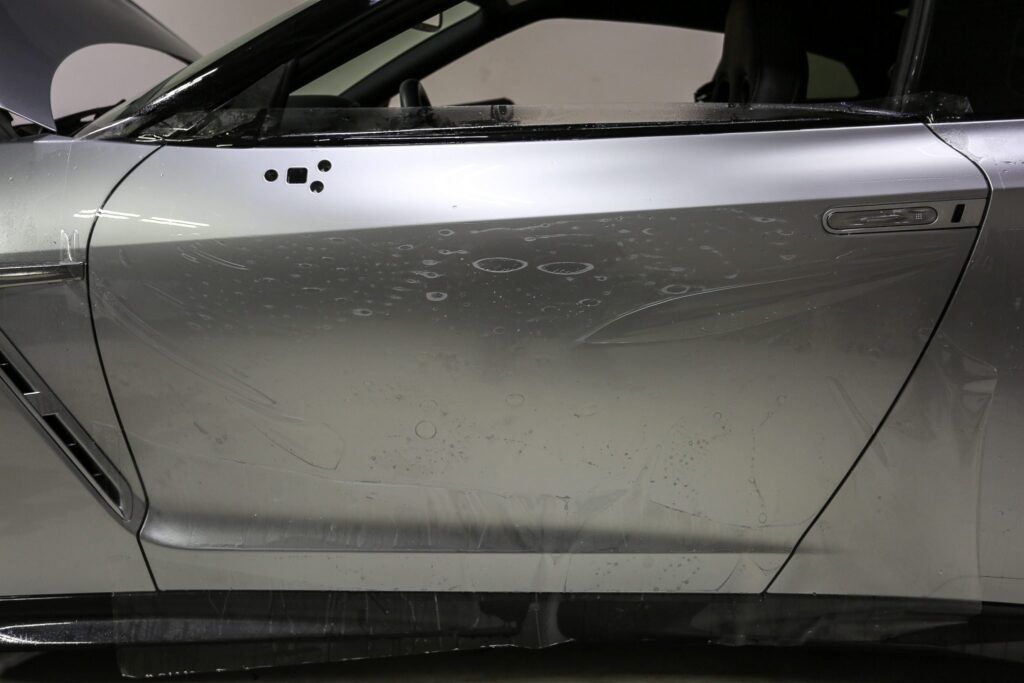 Silver car door with protective wrap; visible scrapes and a vent.