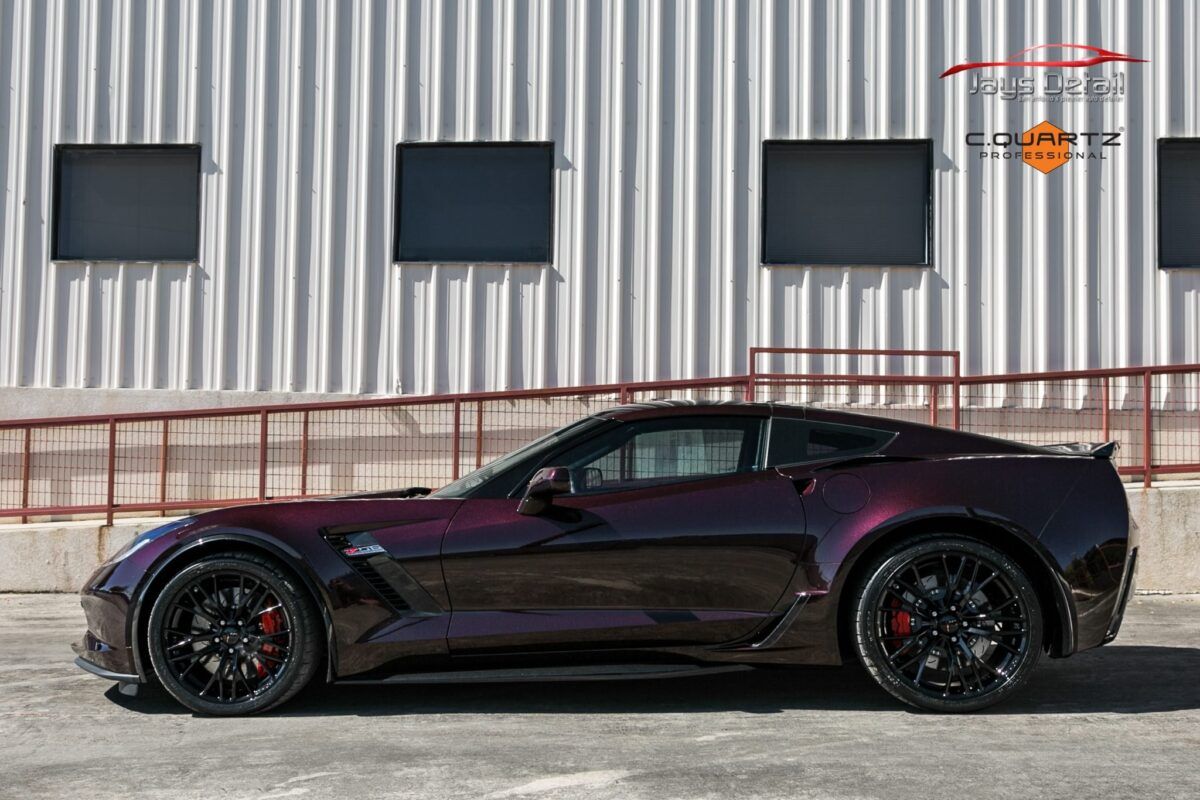 Dark purple Corvette sports car parked in front of a white building with black windows.