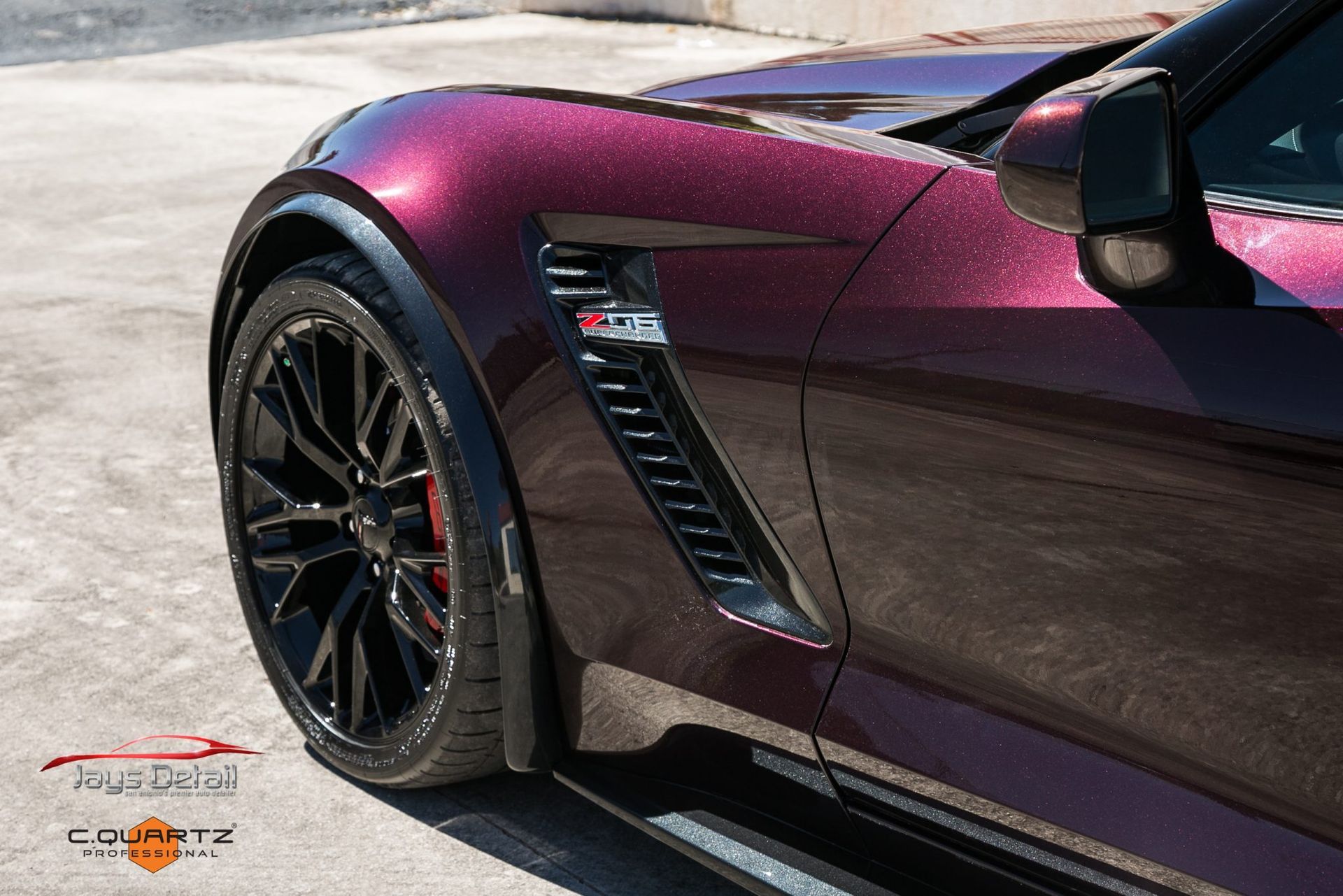 Close-up of a dark purple Corvette's front fender with black wheels, a vent, and the Z06 logo.