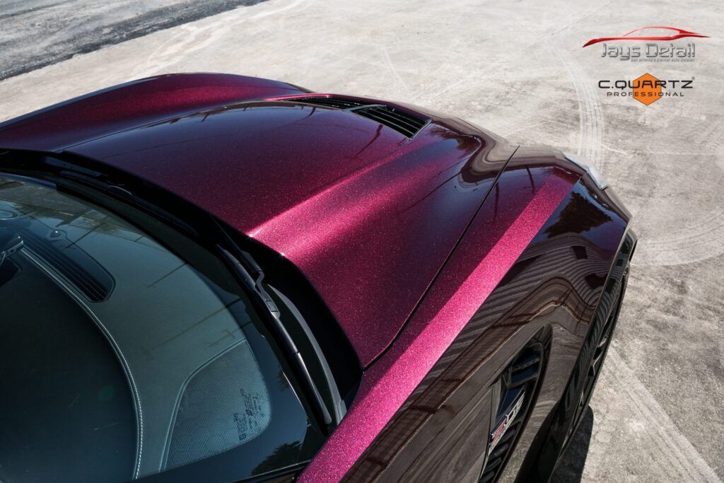 Close-up of a burgundy sports car hood. The car is parked on a paved surface.