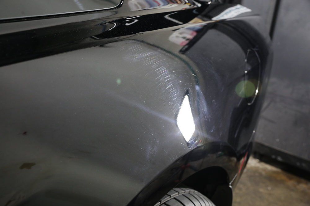 Black car's rear quarter panel with scratches and reflections.