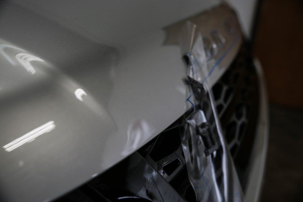 Close-up of a white car's front bumper with protective plastic covering the grill.