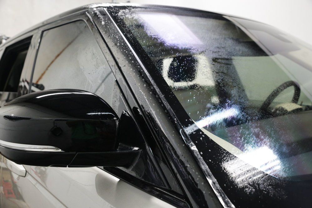 Black car with window film applied to the windshield and side window; wet and reflective.