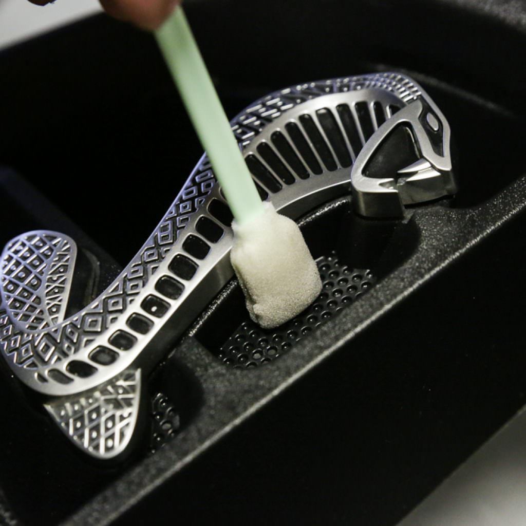 A hand cleaning a silver snake-shaped object with a swab inside a dark container.
