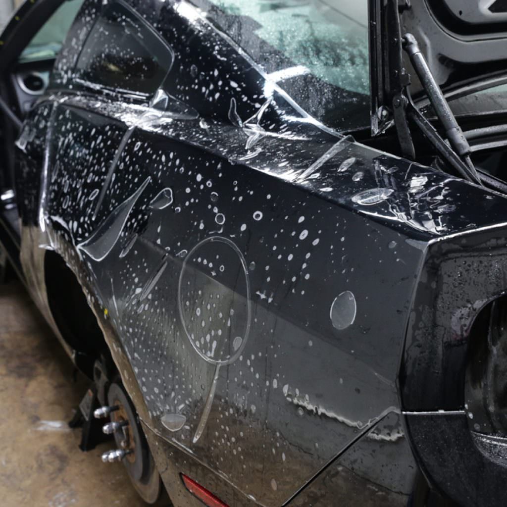 Black car with wet surface, possibly being detailed or wrapped.