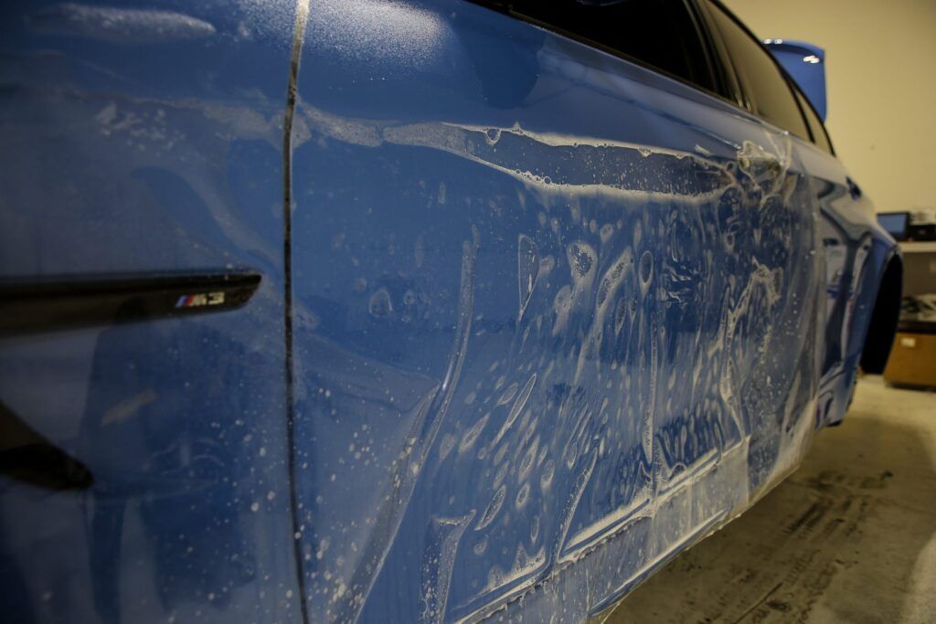 Blue car with clear protective film applied to the side.