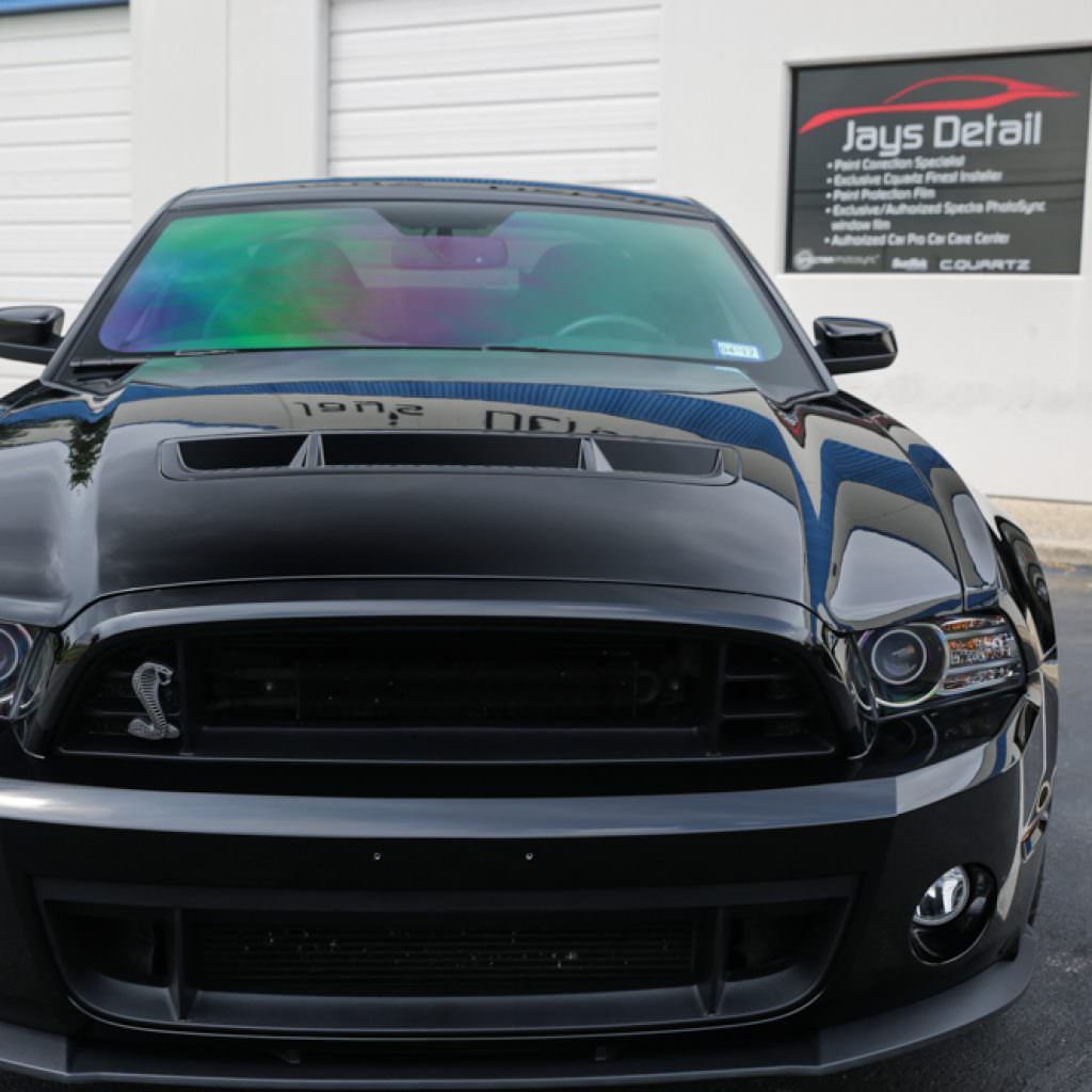 Black Ford Mustang Shelby parked in front of a Jays Detail garage, with multi-colored window tint.