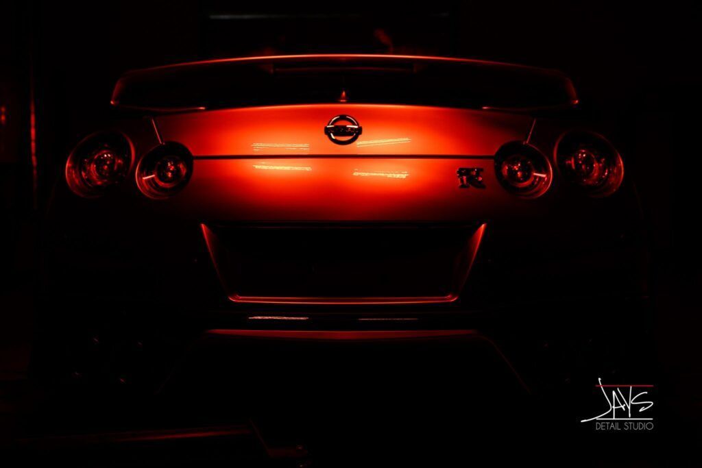 Red-lit rear of a Nissan Skyline, showcasing taillights and logo in a dark setting.