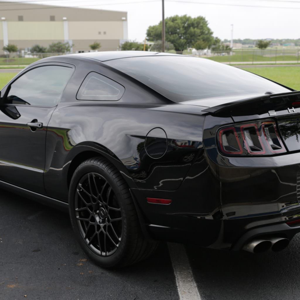 Black Ford Mustang coupe parked outdoors with black wheels and tinted windows.