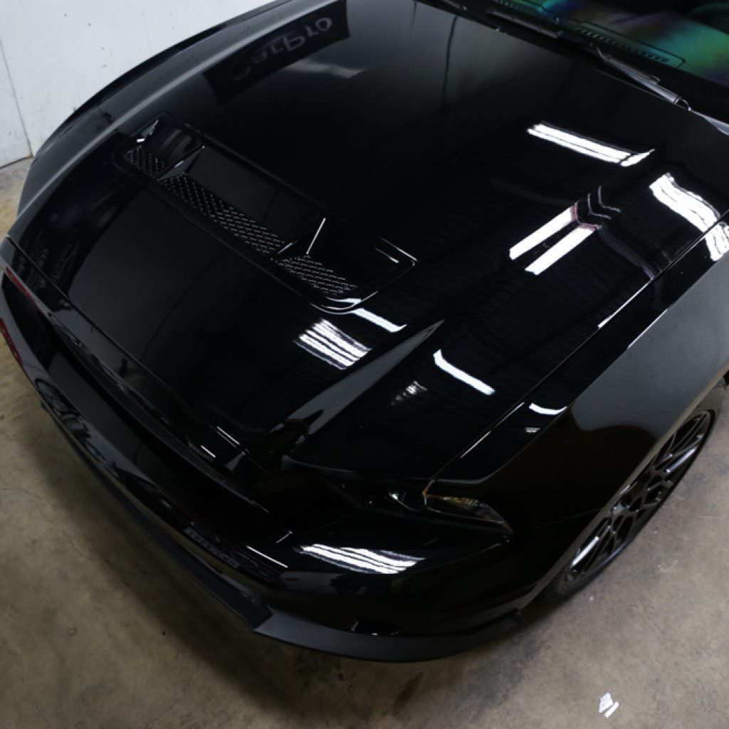 Black Ford Mustang hood with glossy finish, reflecting lights and the surrounding area.