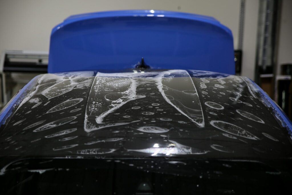 Car roof with soapy bubbles, blue spoiler in the background.
