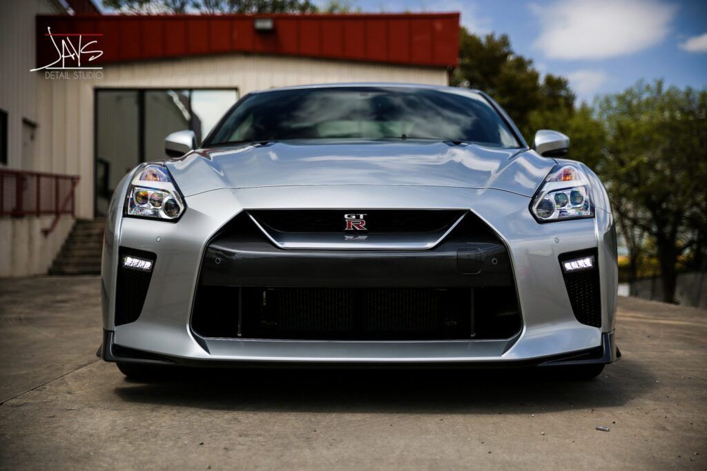 Silver Nissan GT-R sports car parked in front of a building with trees in the background.