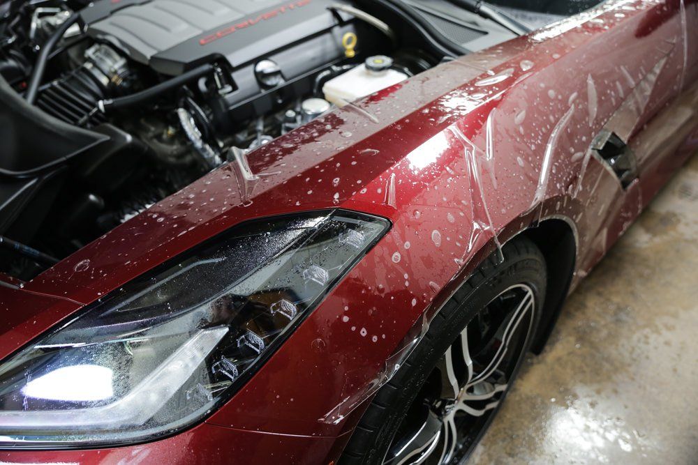 Red sports car with clear protective film on the front fender and headlight, engine visible in the background.