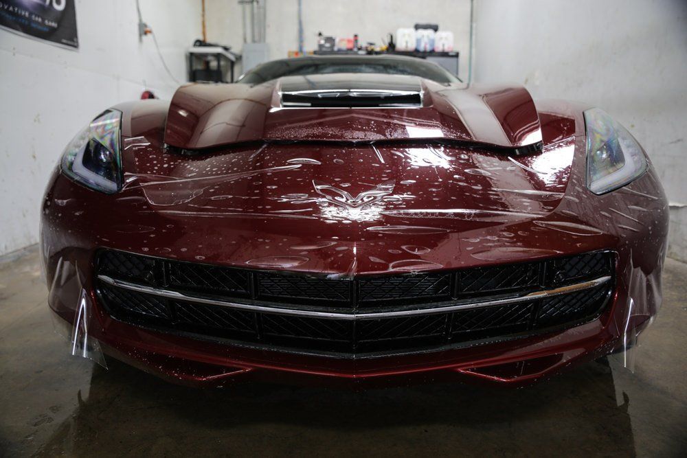 A maroon sports car with soap suds on its hood in a garage.