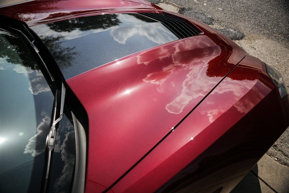 Red car hood reflecting a cloudy sky.