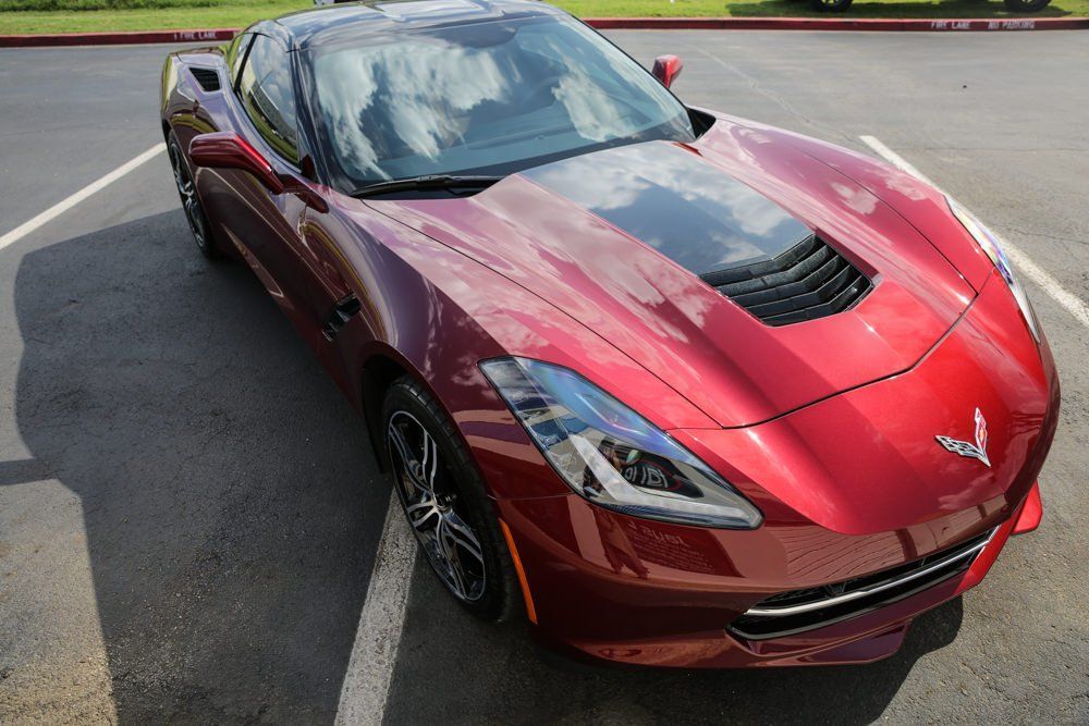 Red Corvette sports car parked in a parking lot, black accents, sunny day.