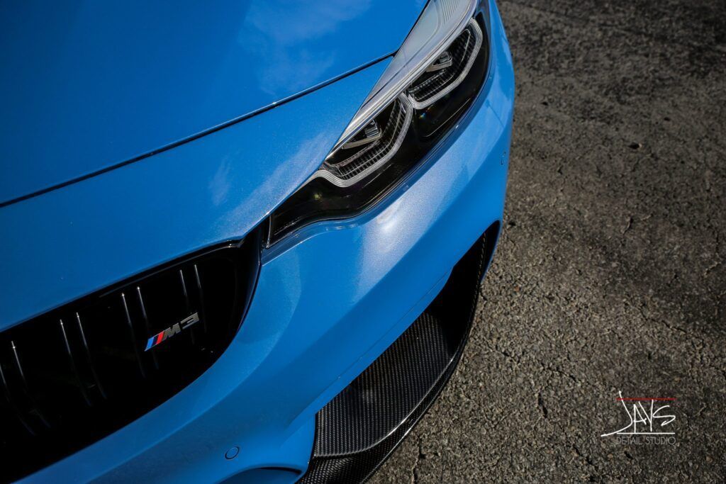 Blue BMW M4 car front with carbon fiber accents, close-up.