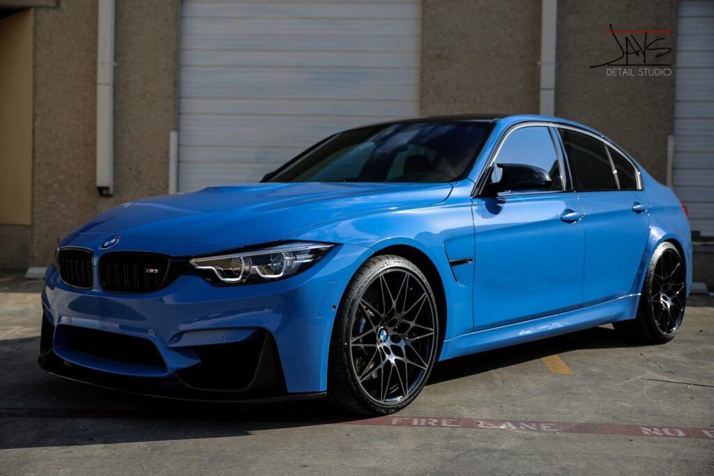 Blue BMW M3 sedan with black wheels parked in front of a building.