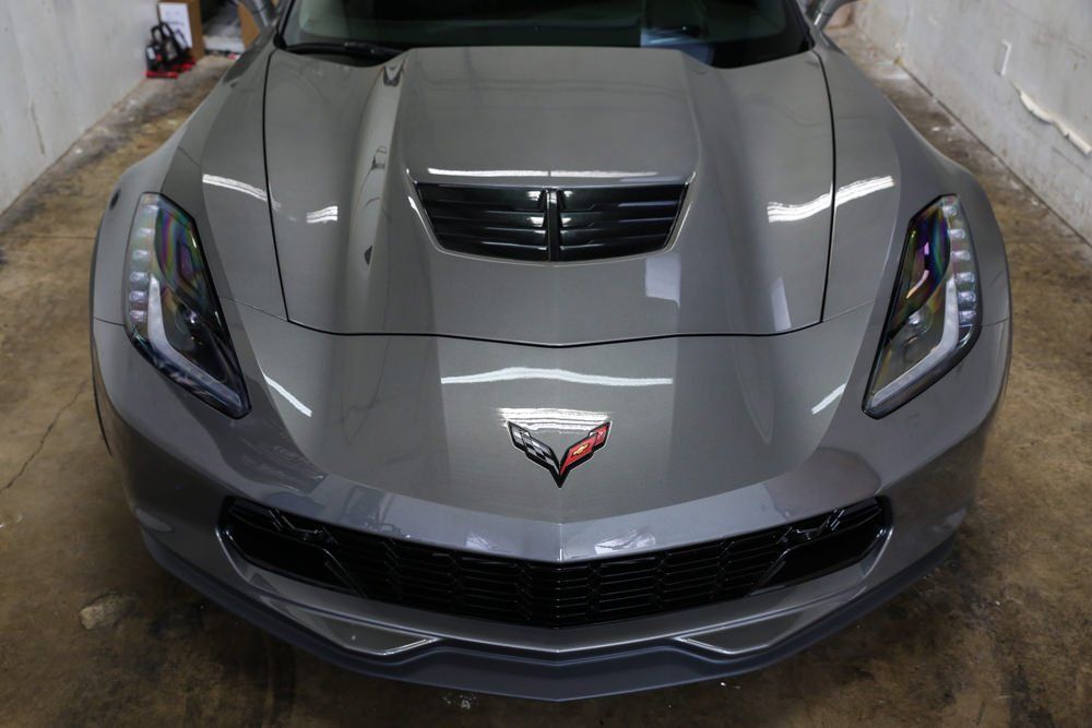 Gray Corvette sports car front view in a garage. The car has a black grill and a Corvette emblem.