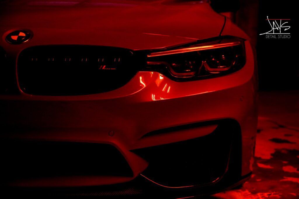Red-lit BMW car front, with black grille and headlights. Dark setting.