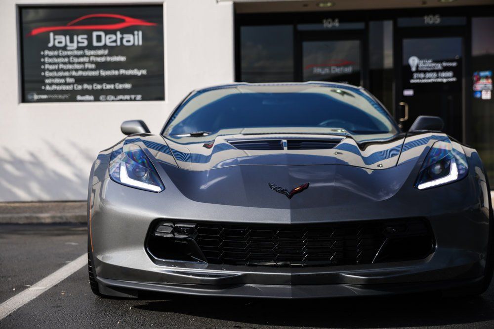 Gray Corvette sports car parked in front of a car detailing shop with services listed on a sign.