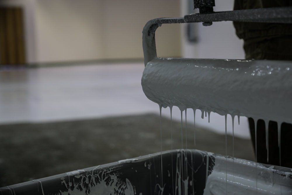 Paint roller dripping gray paint into a paint tray, inside a room.