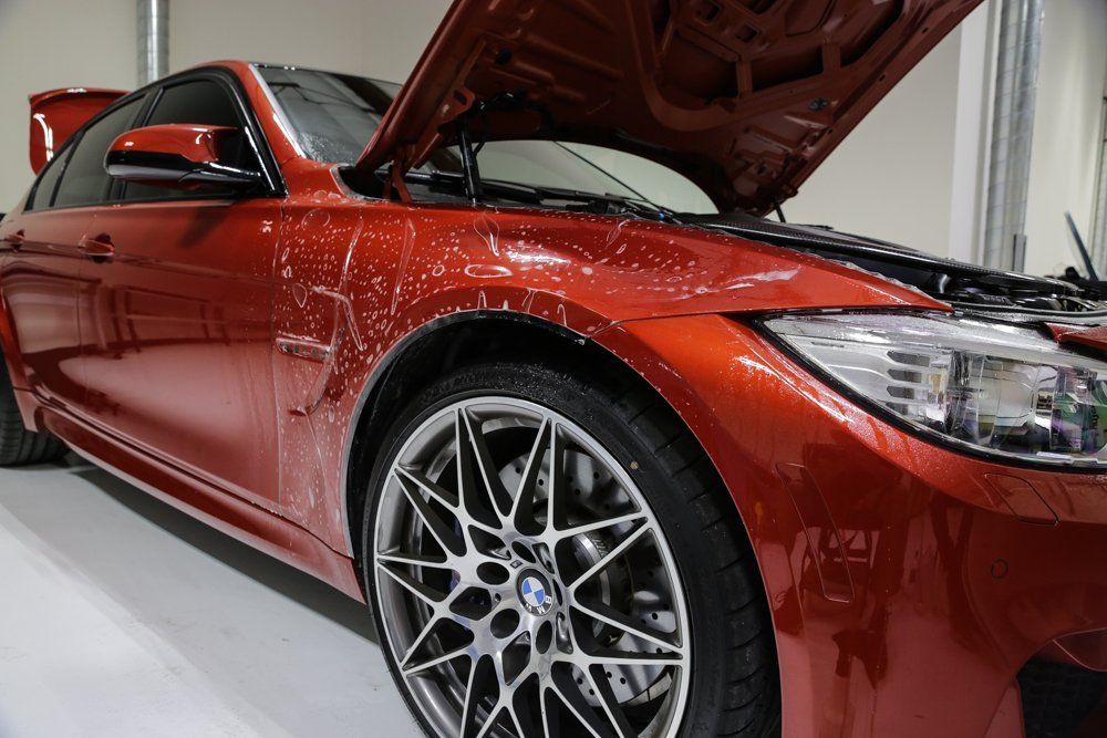 Red BMW sports car with hood up, in a garage, possibly undergoing paint protection film application.