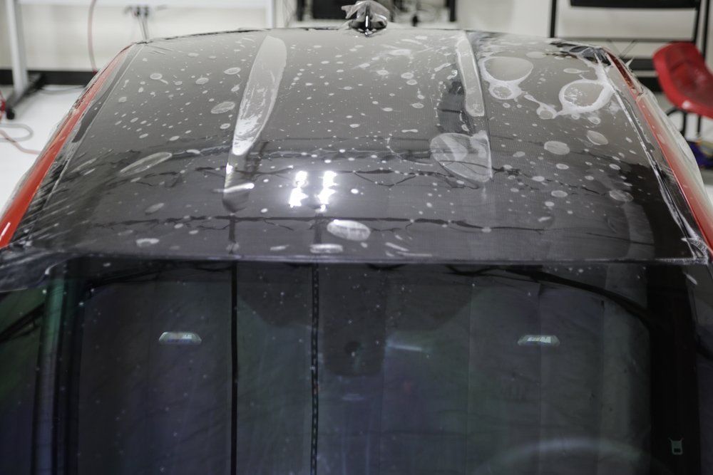 Car roof with protective film being applied, with bubbles visible, indoors.