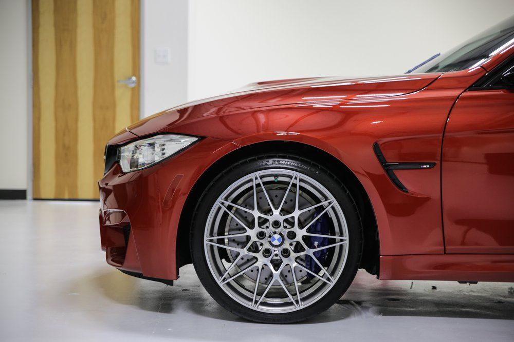 Red BMW M4 sports car parked, front tire and headlight visible.