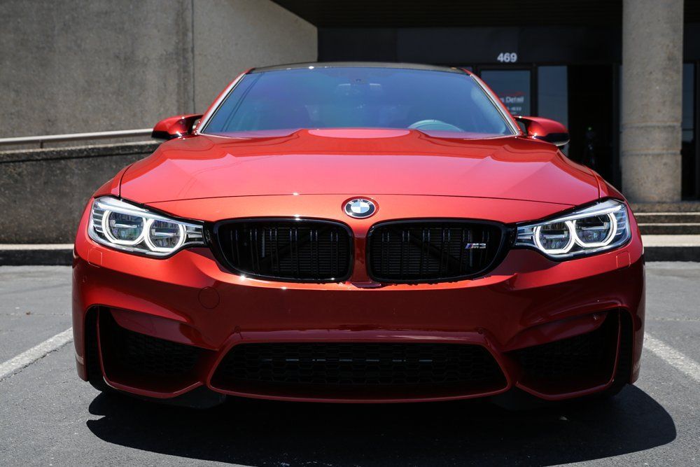 Red BMW M3 sedan parked in front of a building with tinted windows.