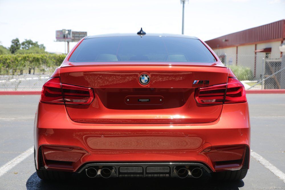 Rear view of a red BMW M3 sedan parked in front of a building on a sunny day.