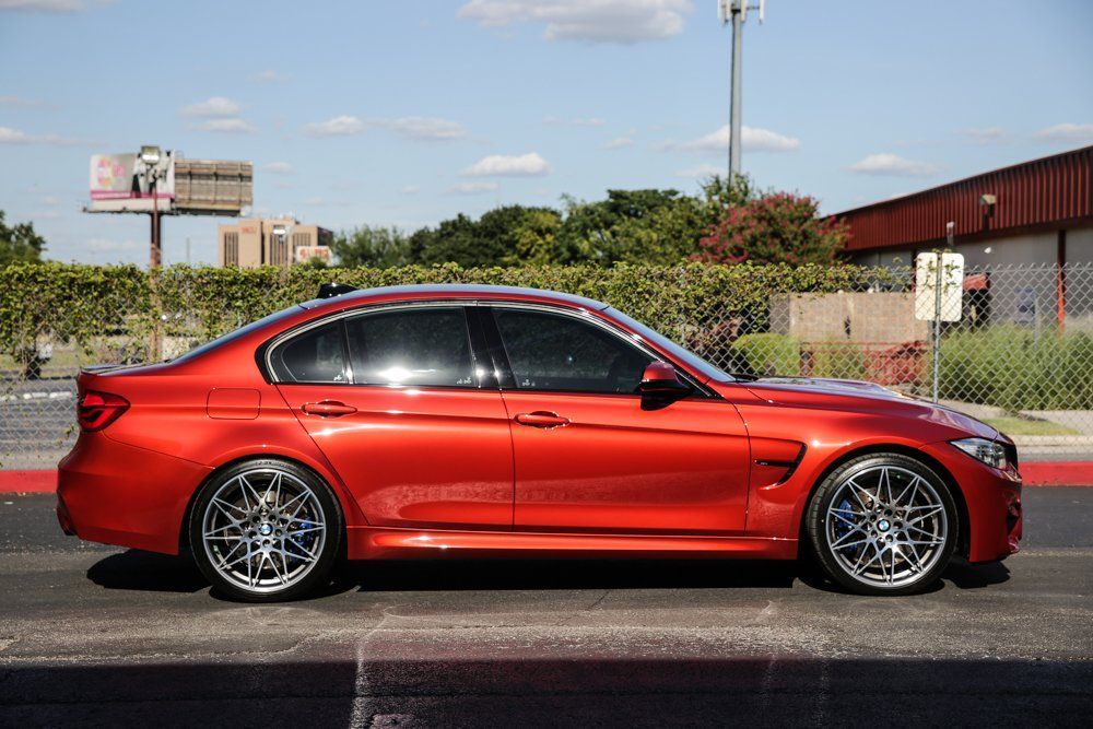 Red BMW M3 sedan with tinted windows and custom wheels parked on a street.