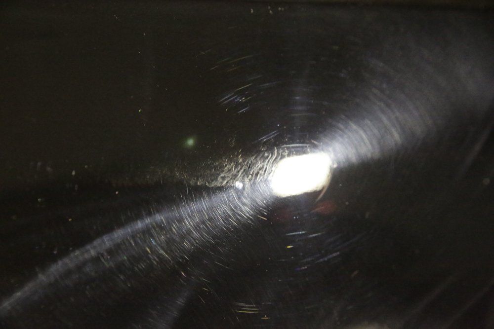 Close-up of a dark surface with swirl marks and light reflections, indicating a polished finish.