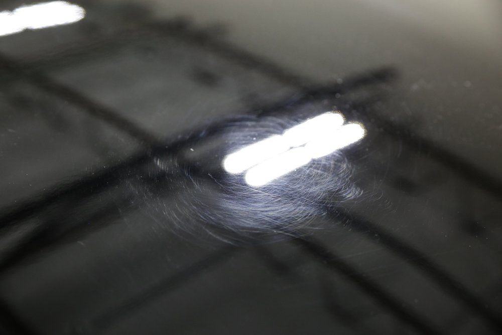 Swirl marks on a shiny black surface, reflecting bright overhead lights.