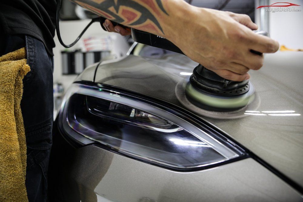 Person polishing car headlight with an electric buffer in a garage.