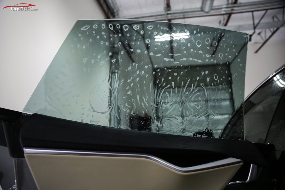 Car window being tinted; film applied with water, bubbles visible. In a workshop, black car.