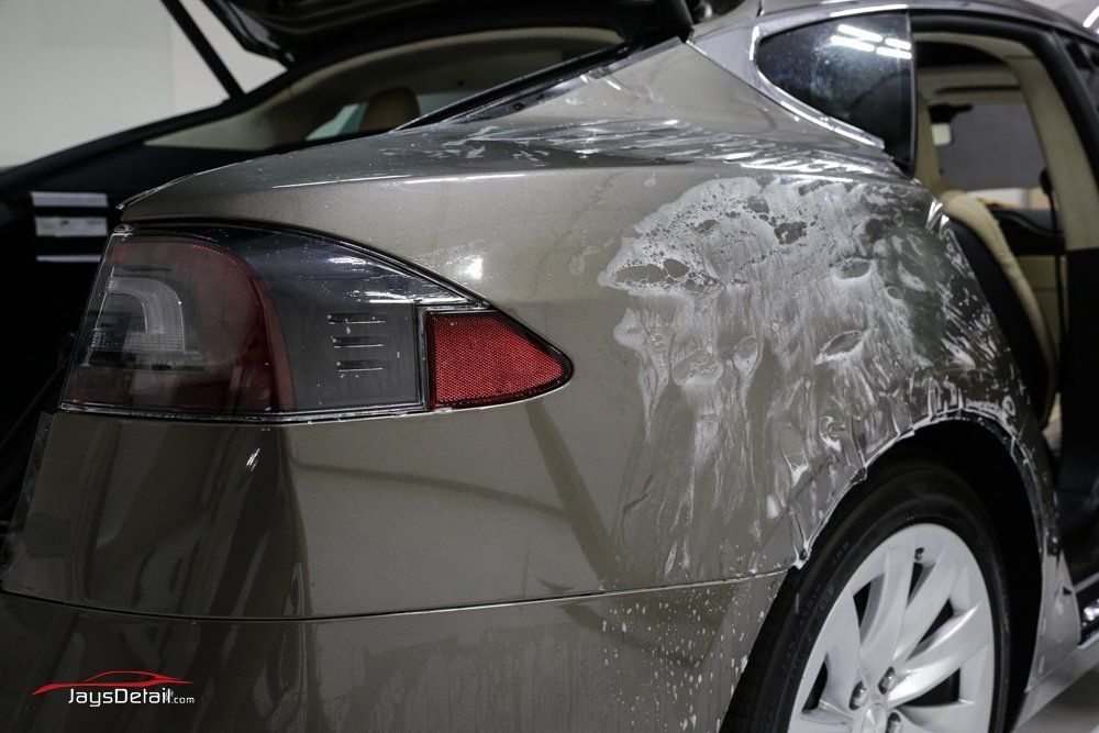 A Tesla Model S being prepped for paint protection film application; soapy residue visible on the rear panel.