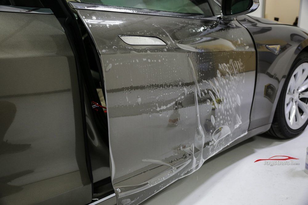 Car with clear protective film applied to the door, showing the process of protecting the paint.