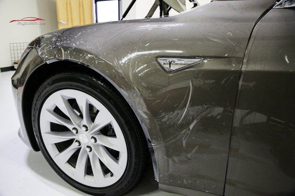 Brown Tesla car with clear protective film on the fender near a white wheel.