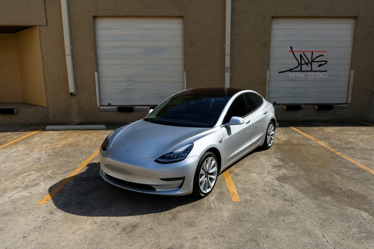 Silver Tesla Model 3 parked in front of a beige building with two garage doors.